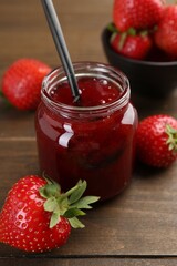 Tasty homemade strawberry jam in glass jar and berries on wooden table, closeup
