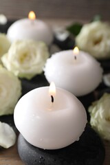 Burning candles, stones and rose flowers on wooden table, closeup