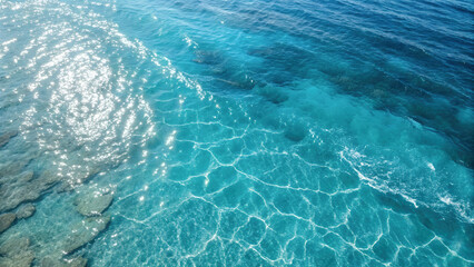 Crystal Clear Blue Ocean Water Surface with Vibrant Turquoise Hues, Sunlight Reflections, and Visible Underwater Pattern