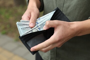 Man putting money into wallet outdoors, closeup