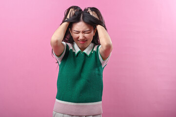 Asian woman pulling her hair in frustration and closing her eyes tightly, expressing extreme stress...