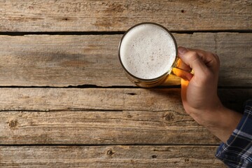 Man with glass mug of beer at wooden table, top view. Space for text