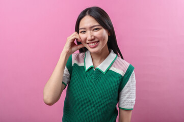 Asian woman smiling and tilting her head while making a heart shape with both hands, wearing a...