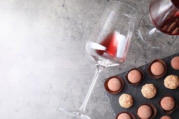 Tasty truffle bonbons and red wine on grey textured table, flat lay. Space for text