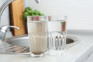 Glasses with clean and dirty water near sink indoors
