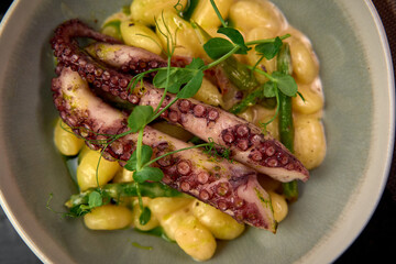Deliciously Prepared Octopus Served on a Bed of Creamy Gnocchi Accompanied by Fresh Green Beans and Garnished with Microgreens