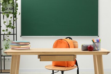 Different school stationery and red apple on wooden table near blackboard indoors