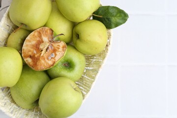 Spoiled apple and good ones in basket on white table, top view. Space for text