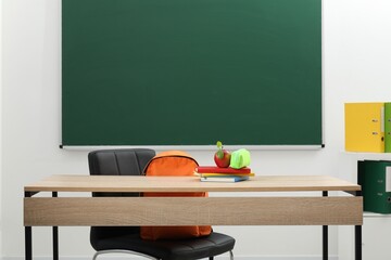 Different stationery and apple on wooden table near blackboard indoors