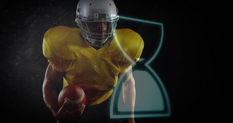 Leaning football player in yellow jersey and grey helmet in studio gripping football with hourglass