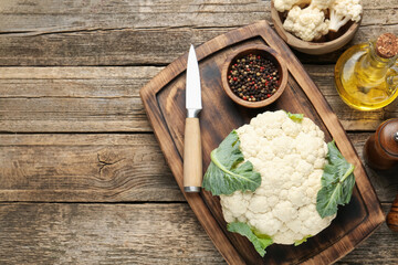 Fresh cauliflower with green leaves, spices and knife on wooden table, flat lay. Space for text