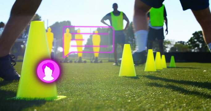 Fototapeta Standing yellow training cones marking pitch, with soccer players practicing near magenta overlays