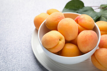 Fresh apricots in bowl on grey textured table, closeup