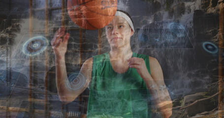 Spinning orange basketball on fingertip, athlete in green jersey at waterfall with digital graphics