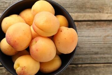 Fresh apricots in bowl on wooden table, top view. Space for text