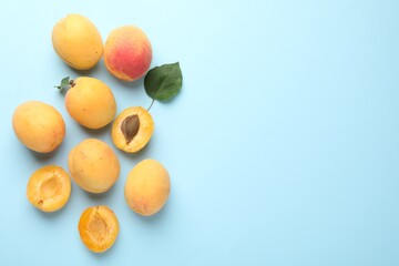 Fresh ripe apricots and green leaf on light blue background, flat lay. Space for text