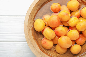 Fresh ripe apricots in bowl with water on white wooden table, top view. Space for text