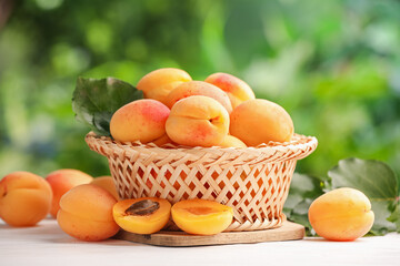 Fresh ripe apricots in wicker basket on white wooden table outdoors