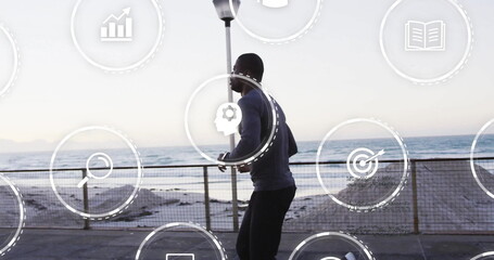 Jogging man wearing sportswear and earphones moving along seaside promenade, with analytics icons