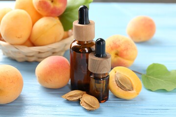 Bottles of essential oil, fresh apricots and kernels on light blue wooden table, closeup