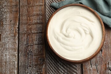 Delicious sour cream in bowl on wooden table, top view. Space for text