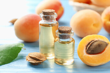 Bottles of essential oil, fresh apricots and kernels on light blue wooden table, closeup