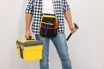 Professional repairman with tool box and hammer on light grey background, closeup