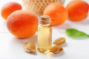 Bottle of essential oil, fresh apricots and kernels on white wooden table, closeup