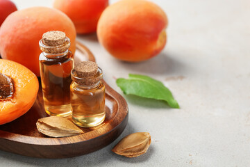 Bottles of essential oil, fresh apricots, kernels and green leaf on light grey table, closeup....