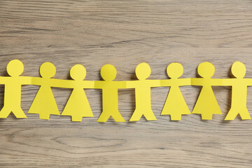 Human paper figures holding hands on wooden background, flat lay