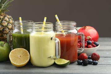 Superfood. Tasty smoothies in mason jars and ingredients on wooden table against grey background,...