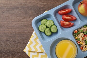 School lunch. Plastic tray with tasty food and orange juice on wooden table, top view. Space for text