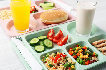 Plastic trays with tasty food, milk and orange juice on light wooden table, closeup. School lunch
