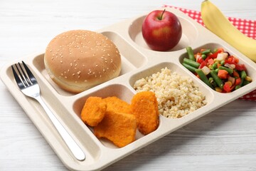 Plastic tray with tasty food and fork on light wooden table, closeup. School lunch