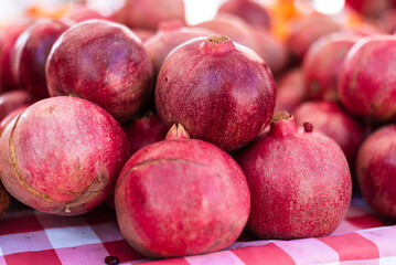 A close-up of a a vibrant red pomegranate from a neatly arranged fruit display at an outdoor farmers market.