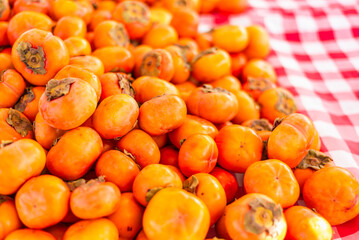 A vibrant display of fresh persimmon fruit arranged neatly for sale at a farmers market, highlighting seasonal produce and tactile interaction with food.