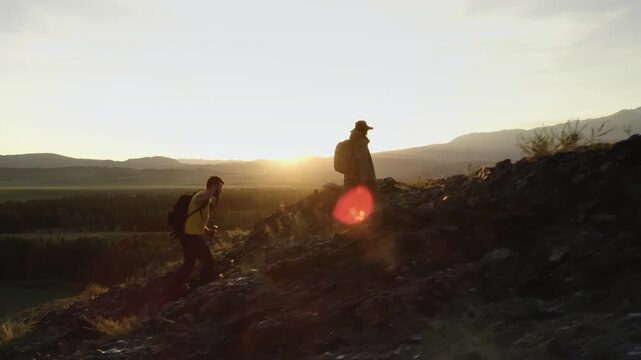 Two young tourists man and woman climb a rocky slope to admire the sunset and beautiful mountain scenery in Altai. Active recreation during summer holidays in nature