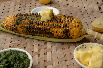 Grilled corn cobs on vintage wood background with lemon, salt, and green chutney or thecha
