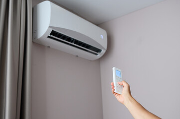 Man holds air conditioner remote control and sets cooling temperature of split system to 17...