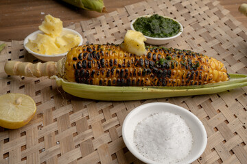 Grilled corn cobs on vintage wood background with lemon, salt, and green chutney or thecha
