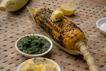 Grilled corn cobs on vintage wood background with lemon, salt, and green chutney or thecha
