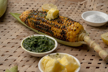 Grilled corn cobs on vintage wood background with lemon, salt, and green chutney or thecha
