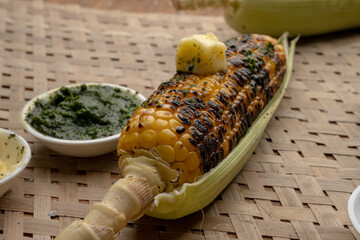 Grilled corn cobs on vintage wood background with lemon, salt, and green chutney or thecha
