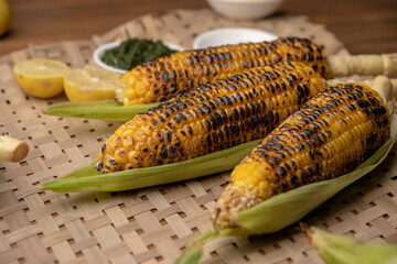 Grilled corn cobs on vintage wood background with lemon, salt, and green chutney or thecha butter
