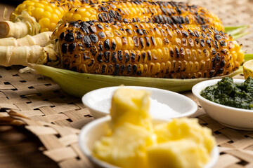 Grilled corn cobs on vintage wood background with lemon, salt, and green chutney or thecha butter
