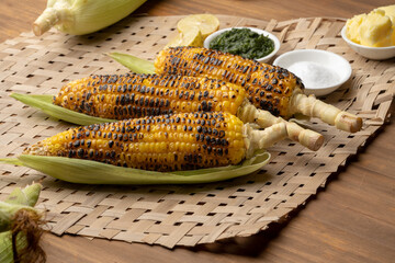 Grilled corn cobs on vintage wood background with lemon, salt, and green chutney or thecha butter
