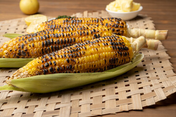 Grilled corn cobs on vintage wood background with lemon, salt, and green chutney or thecha butter
