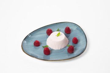 Blancmange, chilled gelatinous sweet dish with raspberries on a plate on a white background