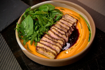 Deliciously plated duck breast served with a vibrant carrot puree and fresh greens, showcasing culinary artistry and mouthwatering flavors in gourmet cuisine.