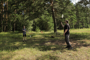 Teenage girl and father standing opposite each other with rackets in hand, focused on shuttlecock in mid-air, summer family activity promoting health and joy.